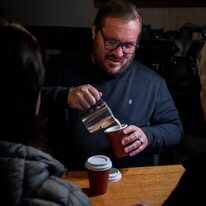 Owner pouring milk into a takeaway coffee with a smile