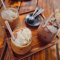 Three iced coffees topped with vanilla ice cream on a wooden tray